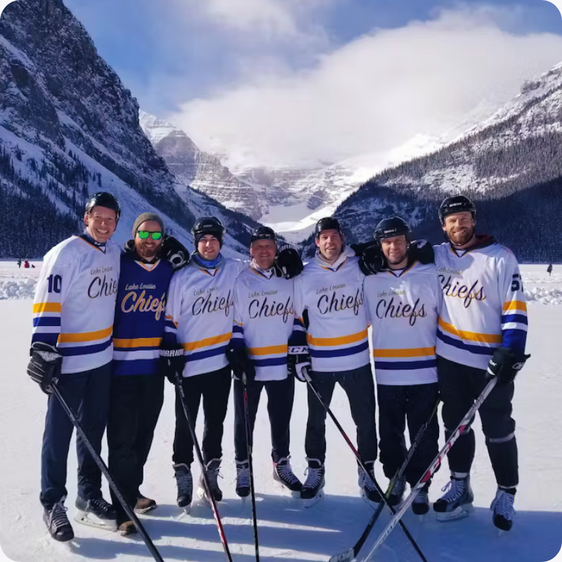 A hockey team with custom Jerseys Made Easy jerseys posing on an outdoor rink in front of mountains.